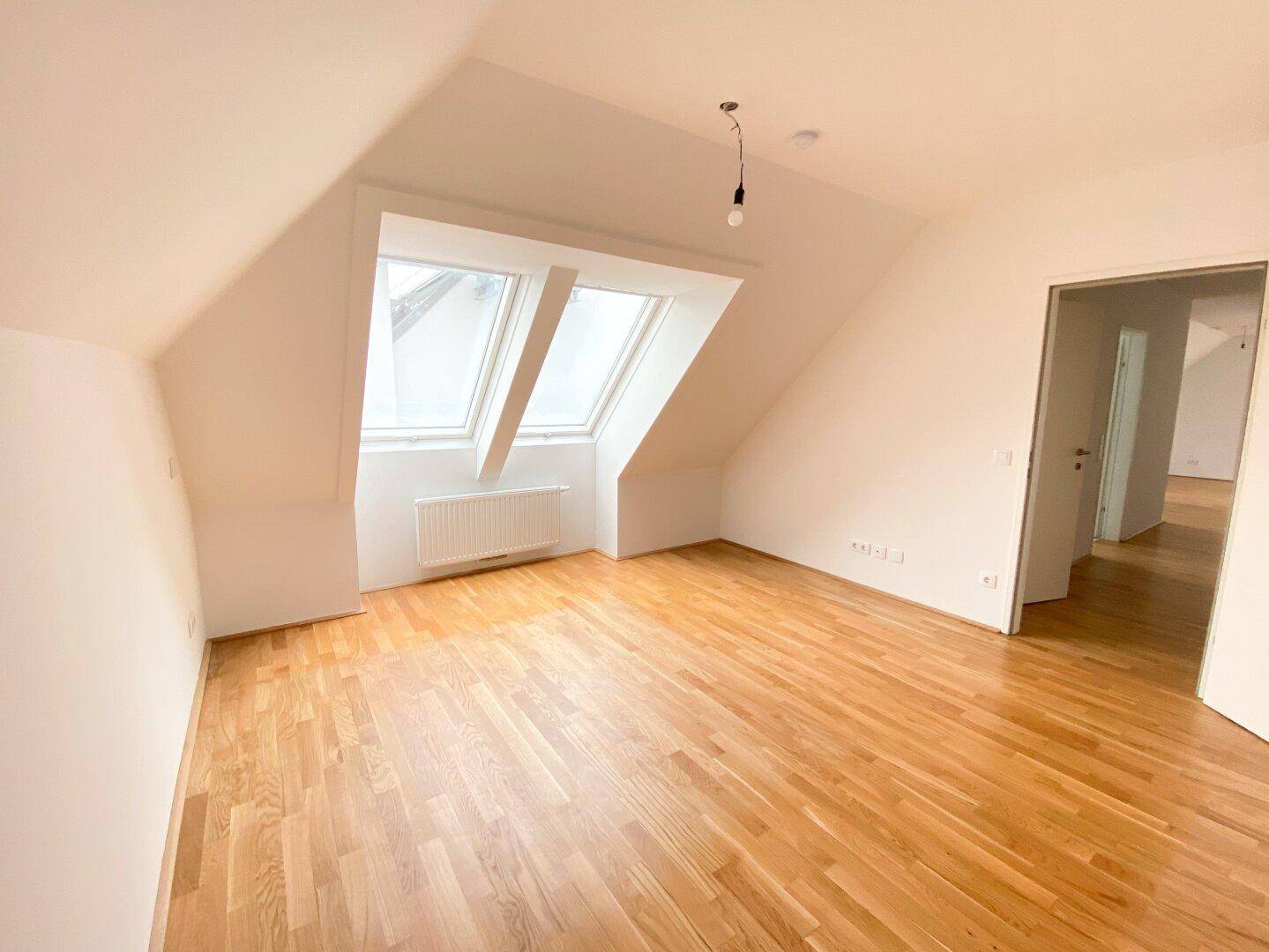 Helles Schlafzimmer mit Parkettboden und zwei großen Dachfenstern unter einer Schräge.