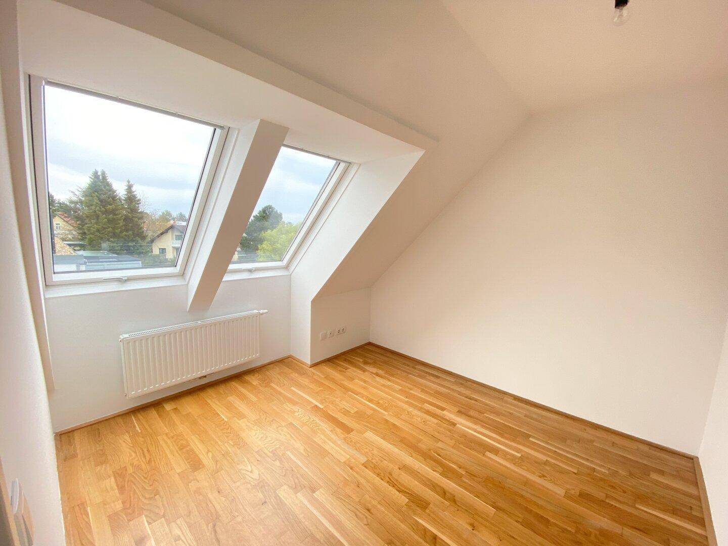 Lichtdurchflutetes Schlafzimmer mit Parkettboden und schrägen Wänden durch Dachfenster.