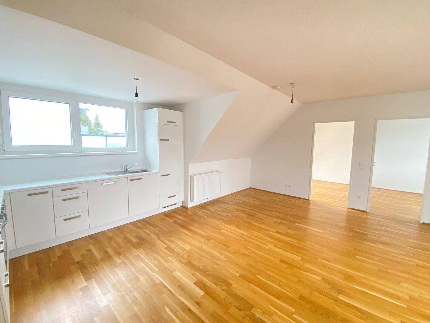 Moderne Einbauküche mit weißen Schränken, Spüle und Fenster in einem hellen Raum.