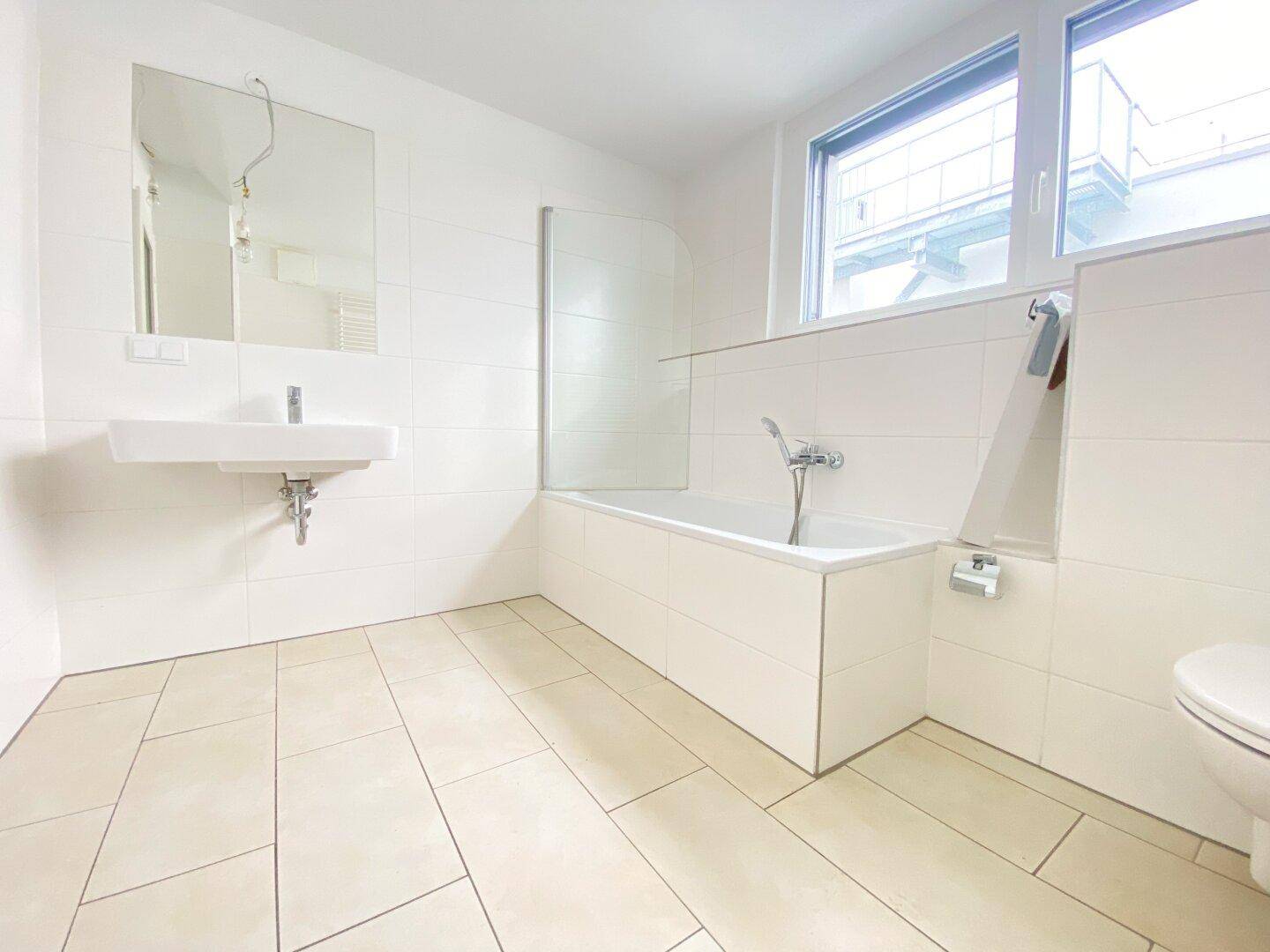 Modernes Badezimmer mit Badewanne, Waschbecken, WC und großen weißen Fliesen.