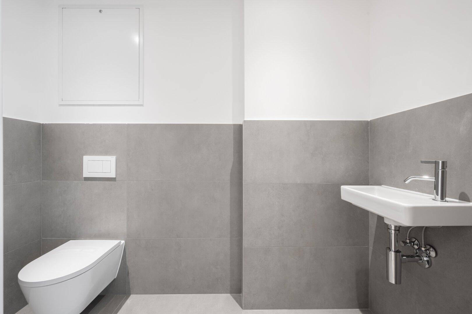 Modernes Gäste-WC mit Wand-WC, kleinem Waschbecken und stilvollen grauen Fliesen.