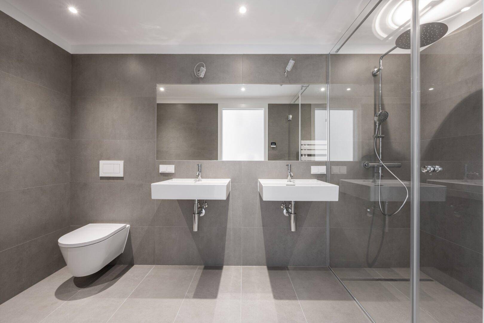 Modernes Badezimmer mit Doppelwaschbecken, großer begehbarer Dusche und eleganten grauen Fliesen.