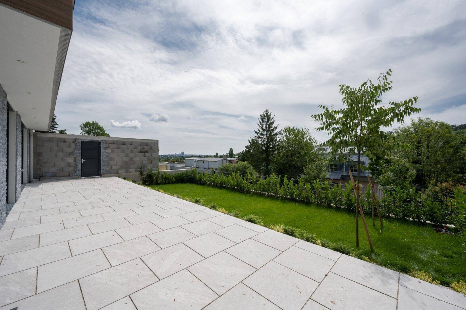 Große, gepflasterte Terrasse mit angrenzender Rasenfläche und Blick ins Grüne.