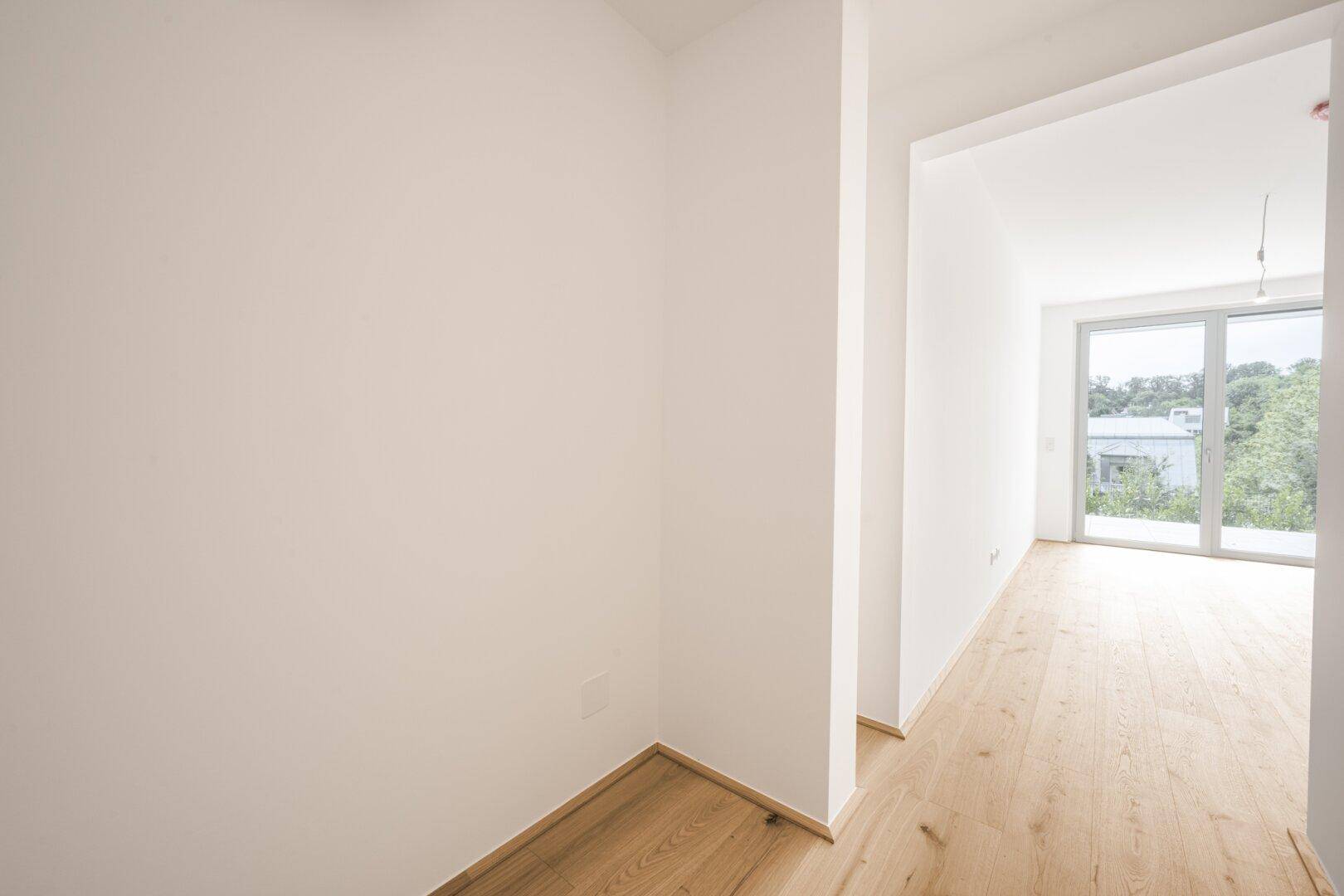 Unmöblierter Raum mit hellem Holzfußboden und Zugang zu einem sonnigen Außenbereich.