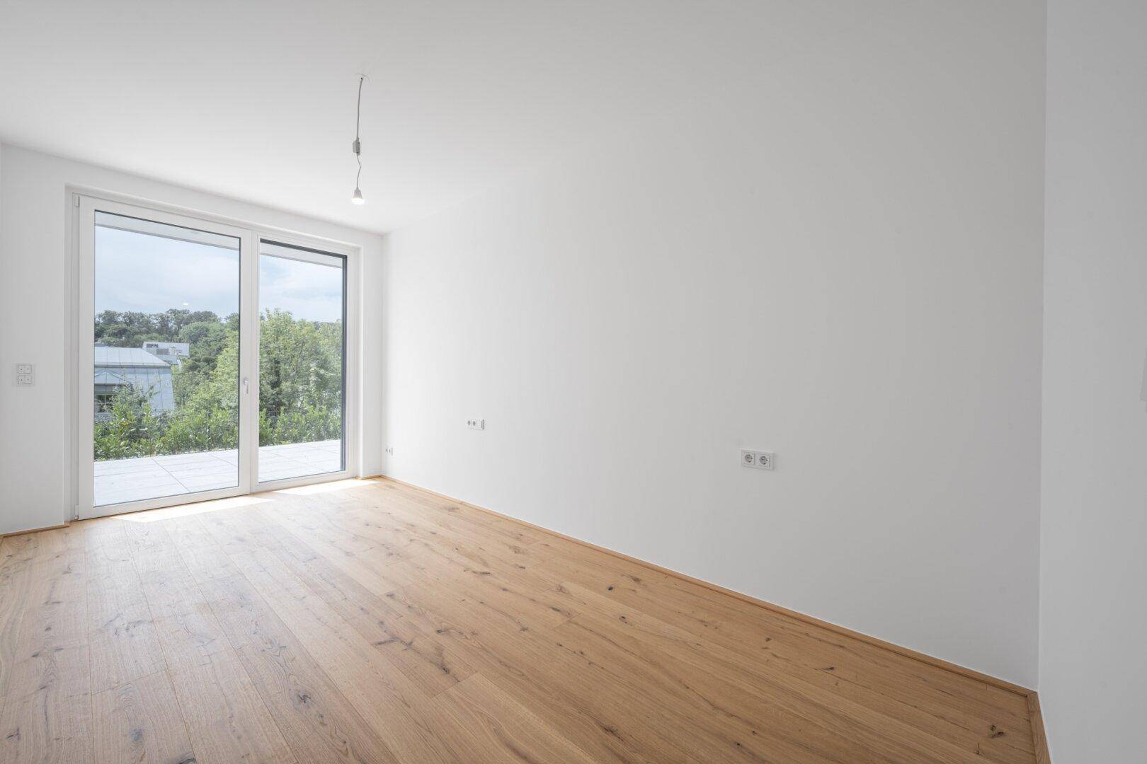 Geräumiger, heller Raum mit Holzboden und breiter Fensterfront für viel Tageslicht.