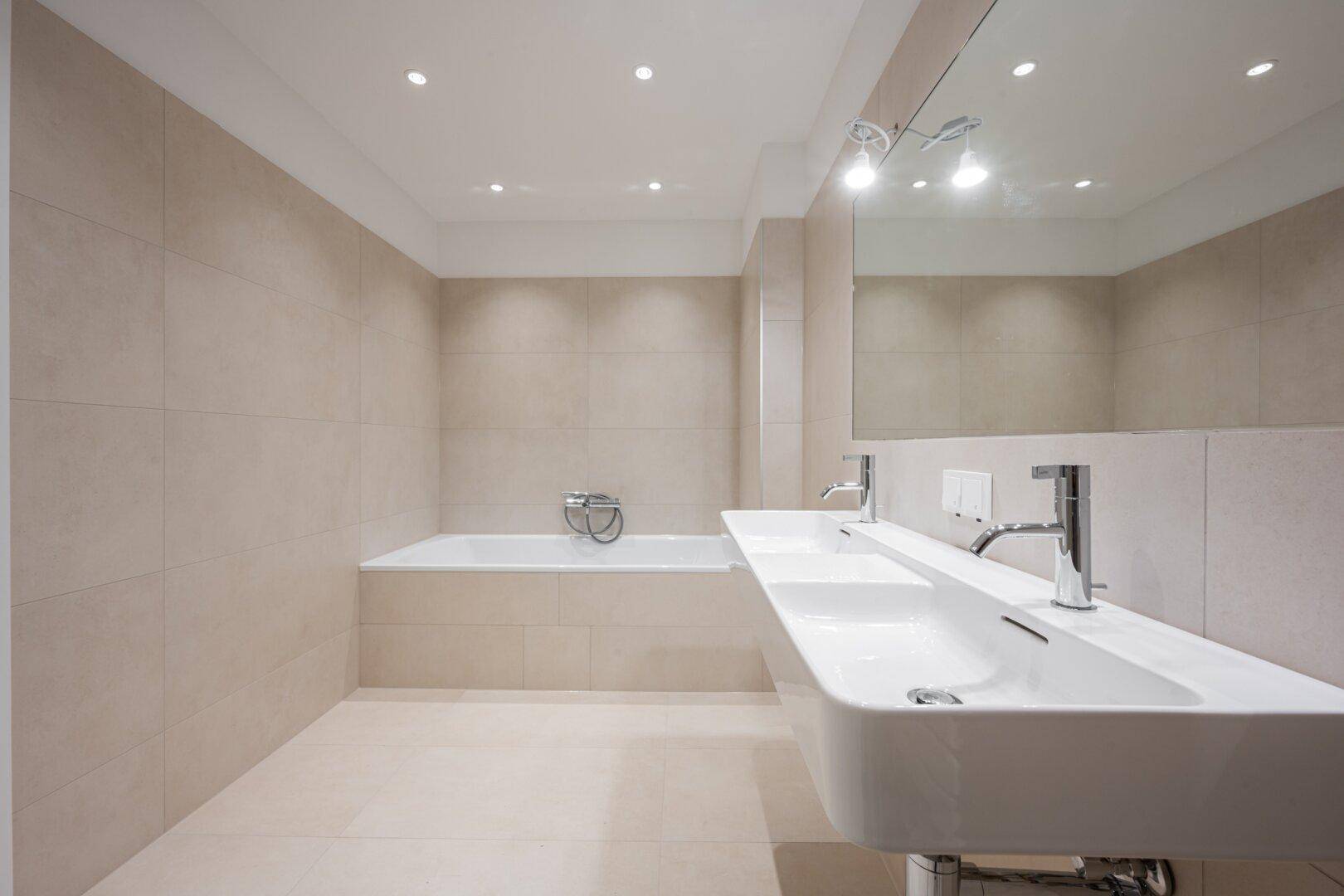 Elegantes Badezimmer mit Doppelwaschbecken, integrierter Badewanne und modernen Armaturen.