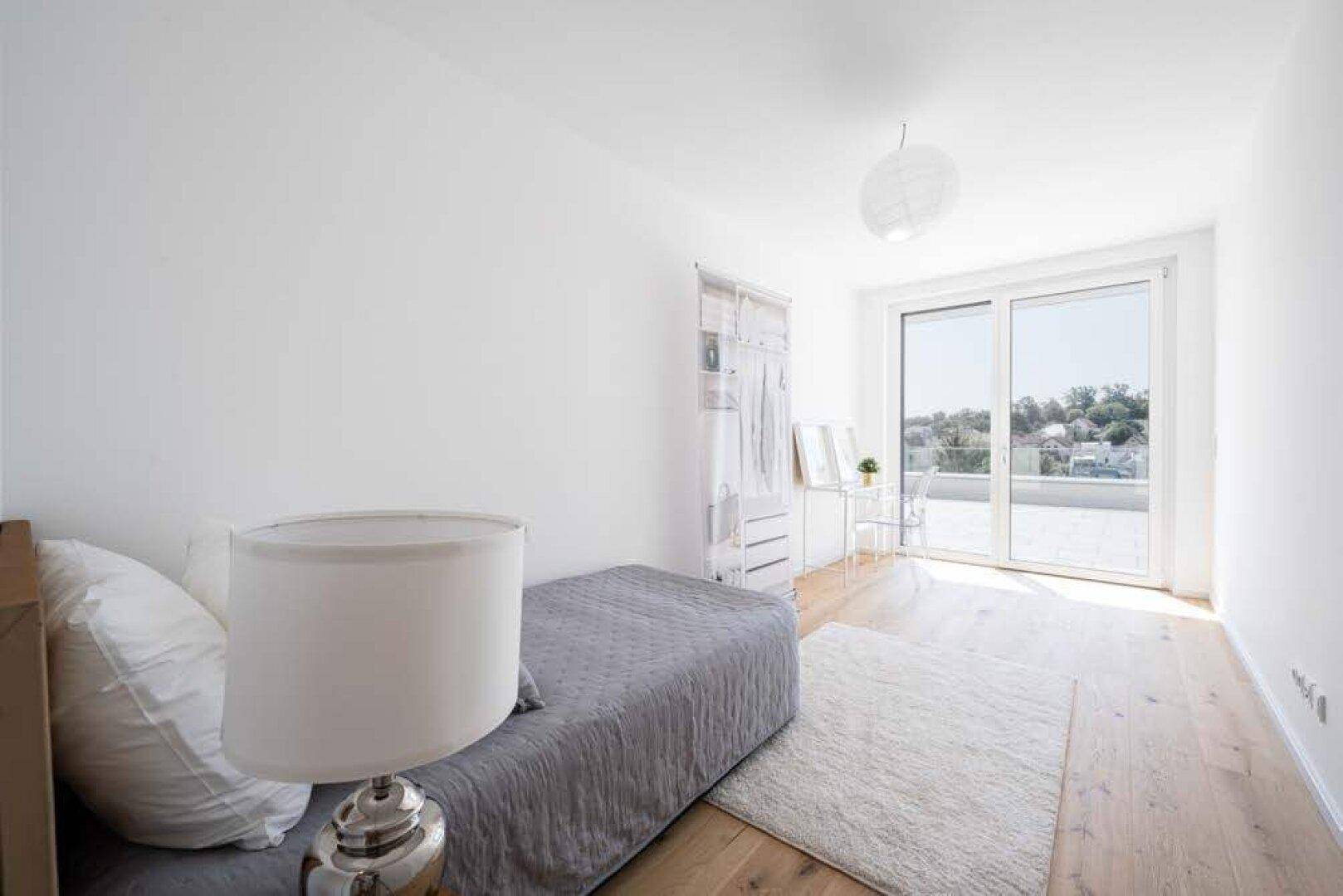 Helles Schlafzimmer mit Holzboden, Teppich und direktem Zugang zur großen Terrasse.