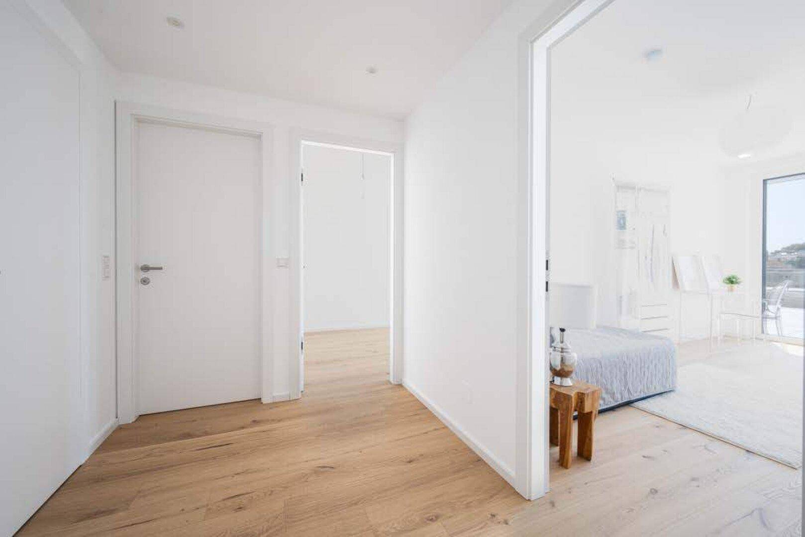 Heller Flur mit Holzboden, der zu einem Schlafzimmer und weiteren Räumen führt.