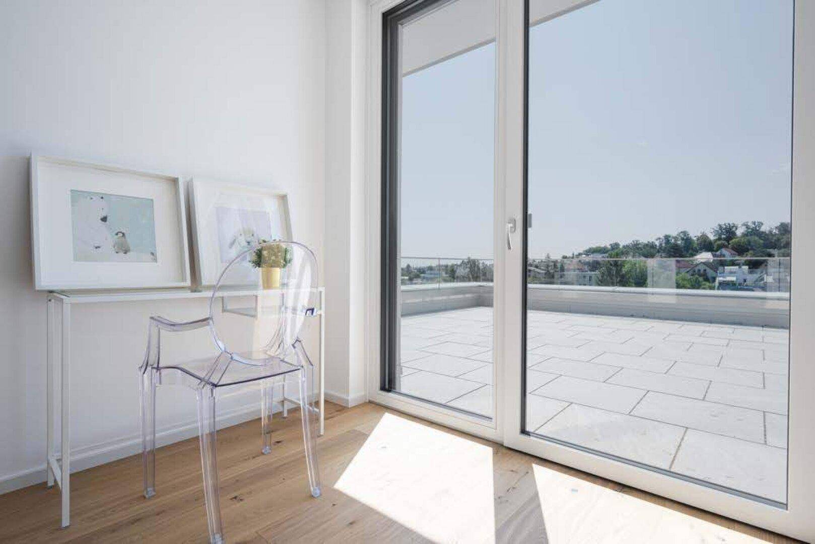 Helles Zimmer mit Holzboden, Schreibtisch und großem Fenster mit Zugang zur Terrasse.