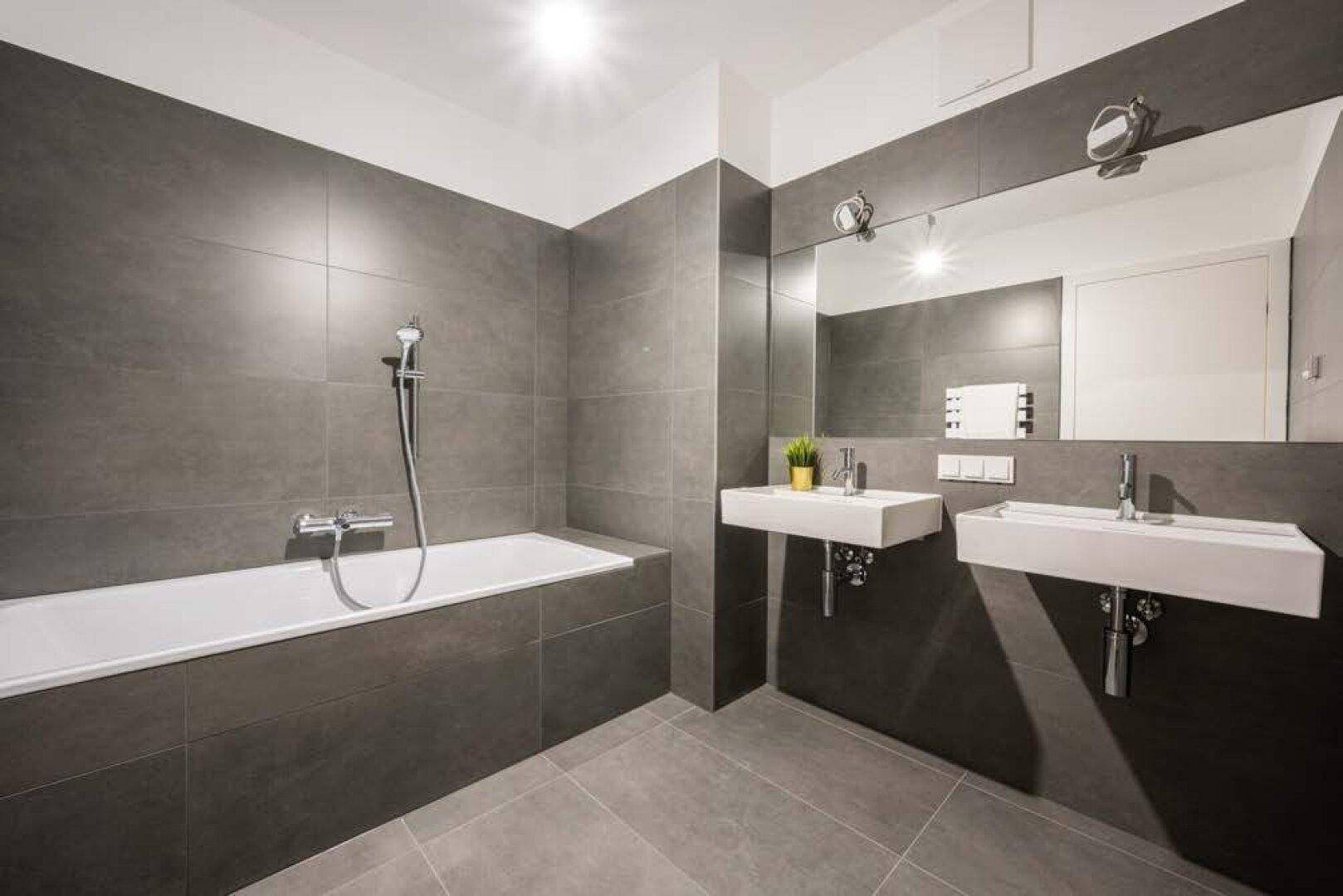 Modernes Badezimmer mit grauen Fliesen, Badewanne und zwei Waschbecken.