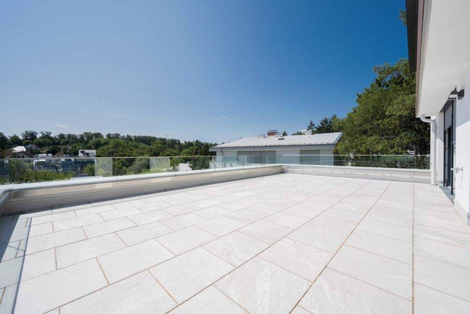 Geräumige Dachterrasse mit Fliesenboden und Glasgeländer, bietet weite Ausblicke.