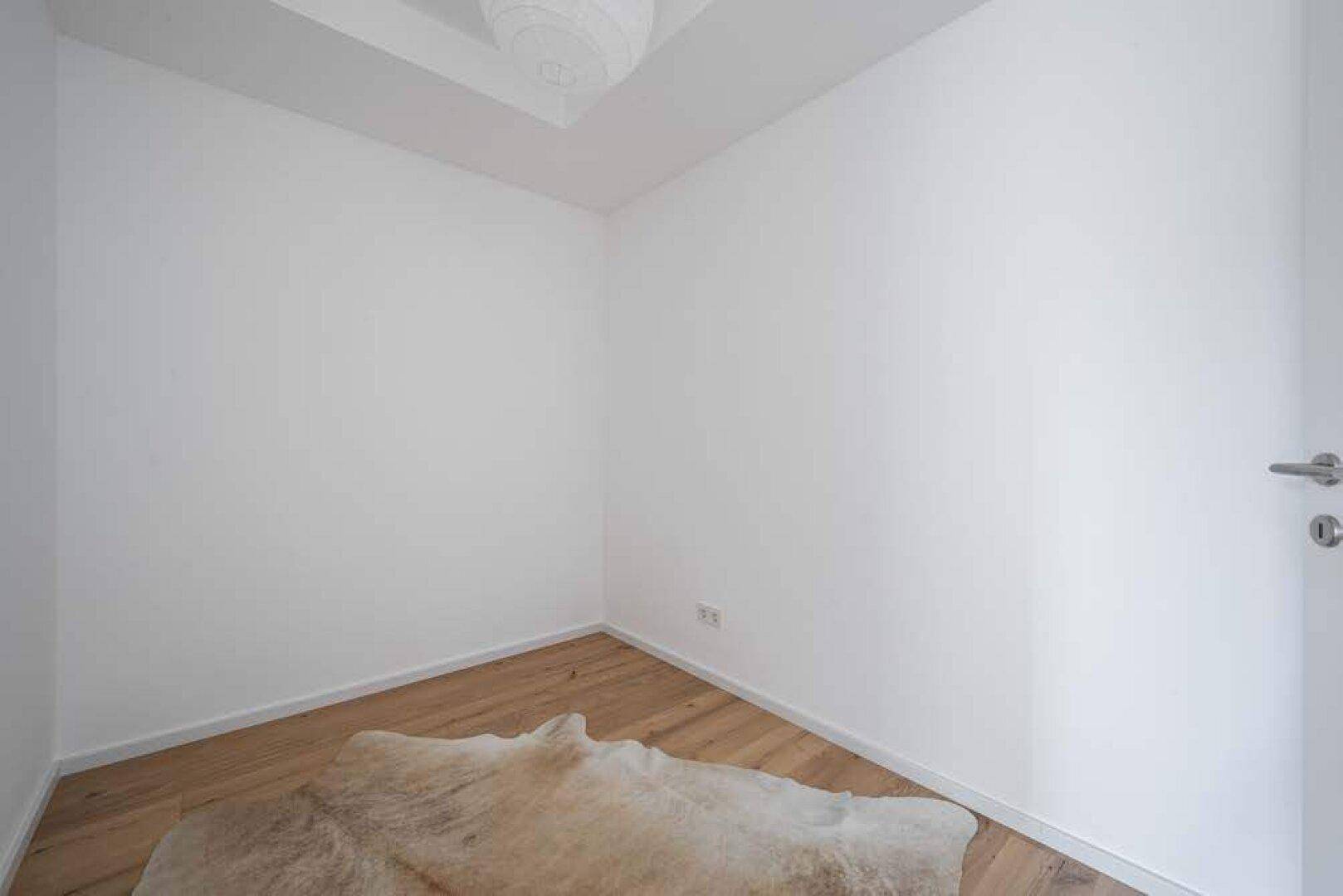 Kleiner, heller Raum mit Holzboden und einem Teppich, vielseitig nutzbar.