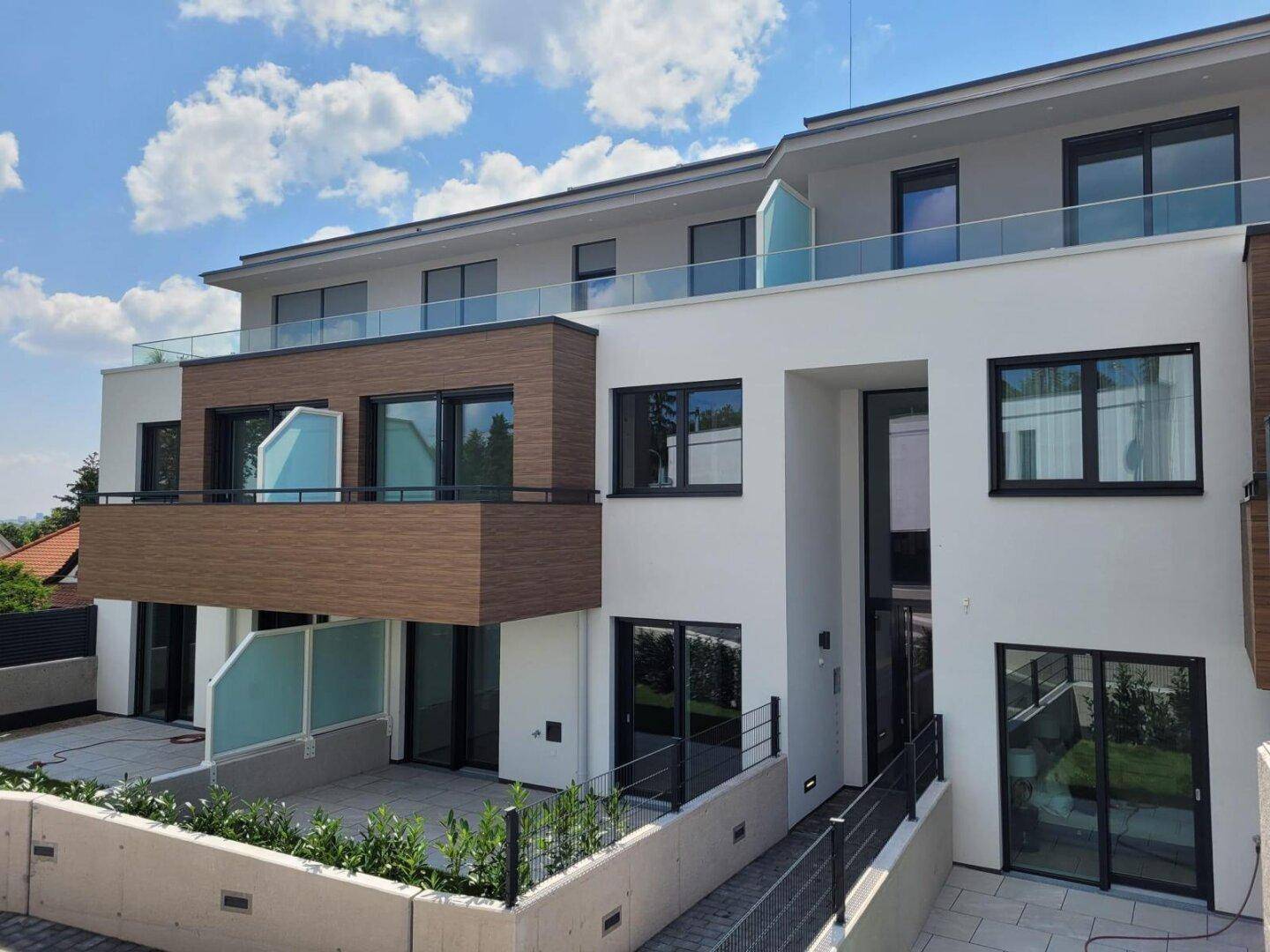 Moderne Wohnanlage mit Terrassen und Balkonen, umgeben von Grünflächen unter blauem Himmel.