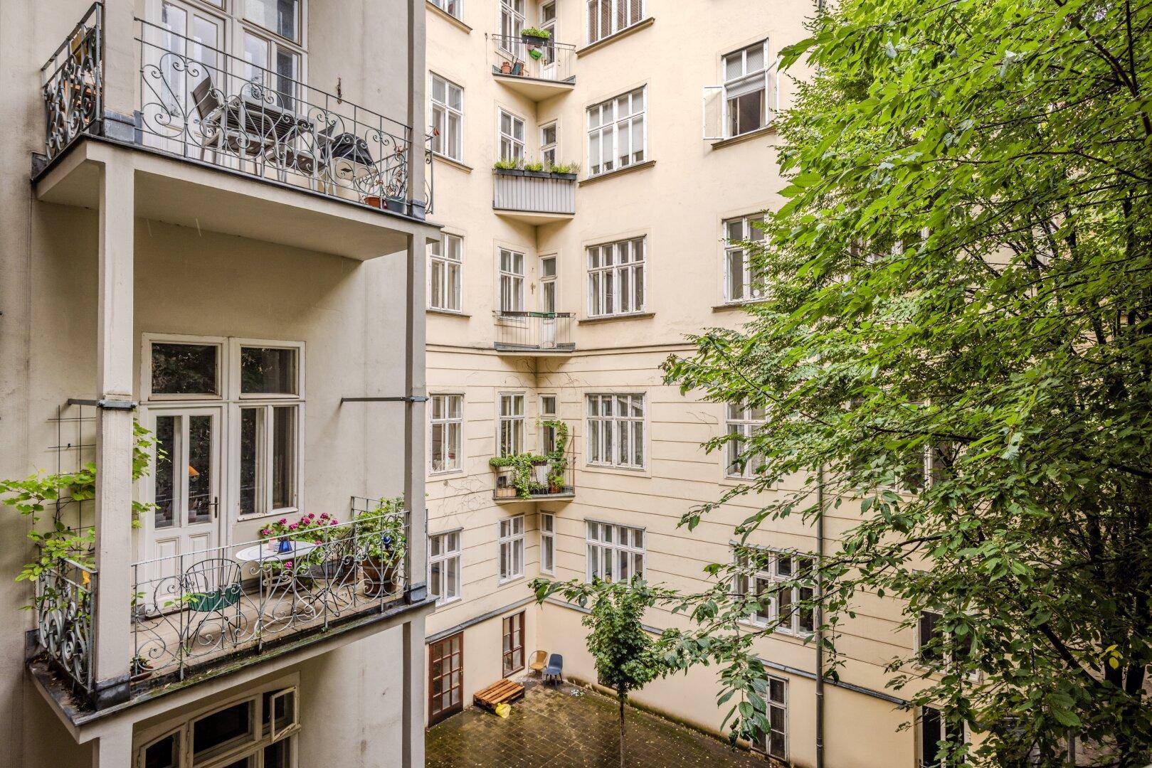 Blick in einen begrünten Innenhof mit mehreren Balkonen und Sitzgelegenheiten.