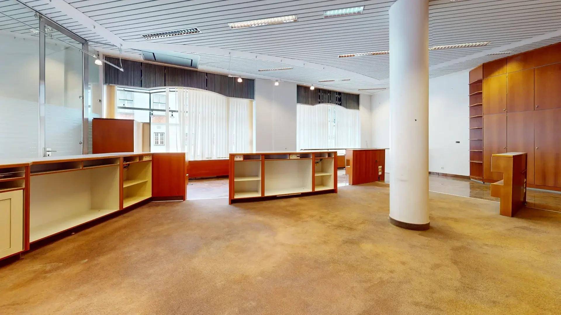 Großer offener Bürobereich mit Teppichboden, Holzmöbeln und großen Fenstern mit Vorhängen.