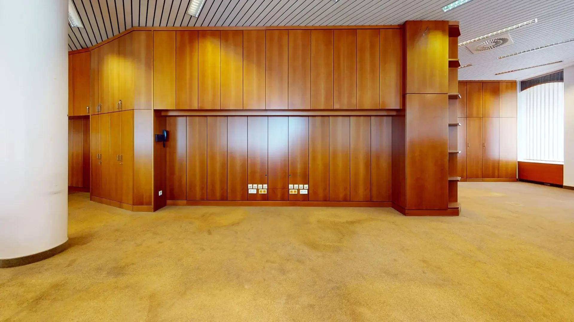 Wand mit durchgehender Holzvertäfelung und integrierten Schränken in einem geräumigen Bürobereich.