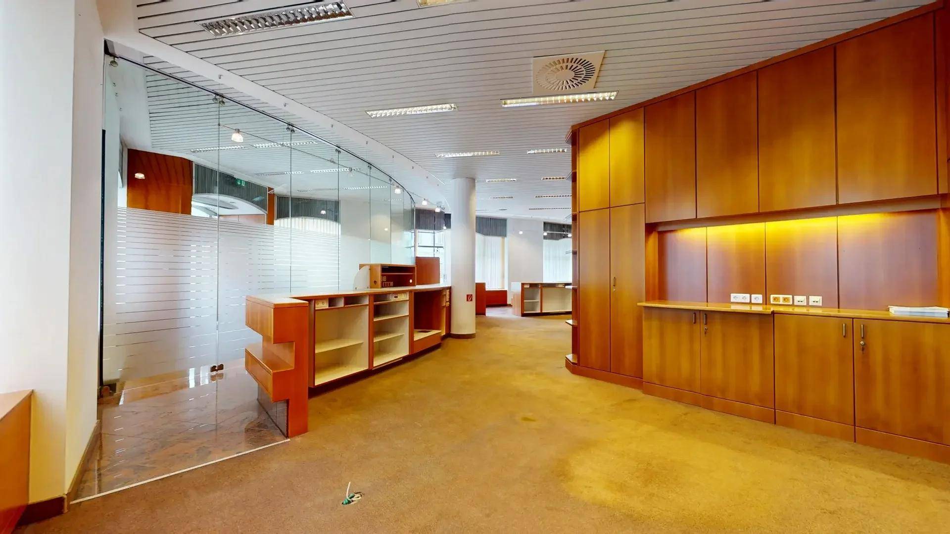 Moderner Bürobereich mit geschwungenen Glaswänden, Holzmöbeln und Teppichboden.