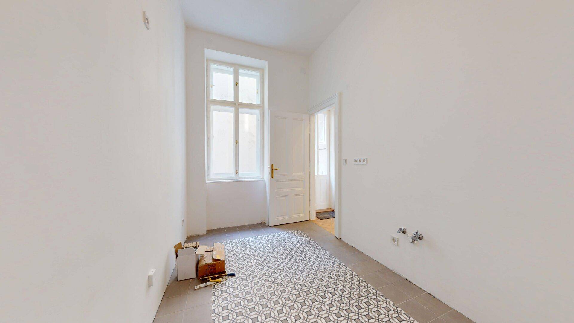 Heller Raum mit Fenster, modernen Fliesen und Anschlüssen, bereit für die Installation einer Küche oder Waschküche.
