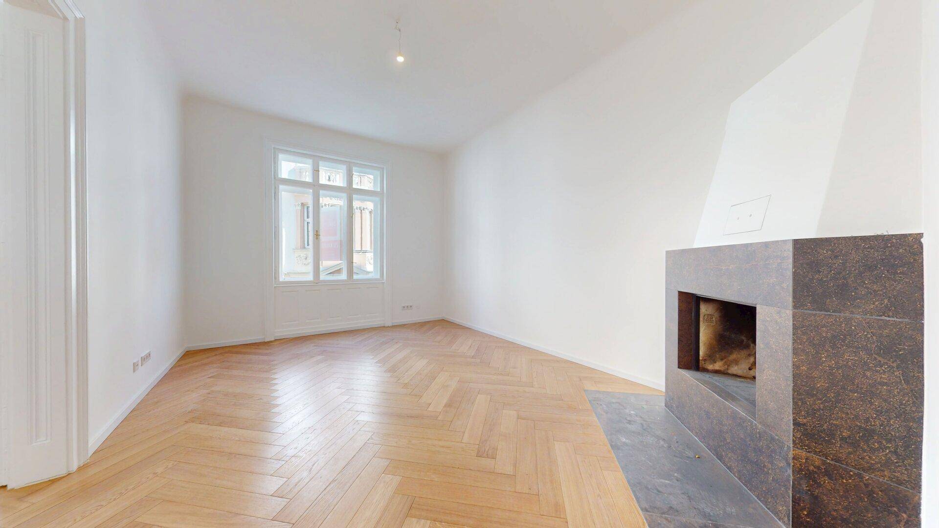 Gemütliches Wohnzimmer mit Kamin, Fischgrätparkett und großem Fenster, das viel Licht hereinlässt.