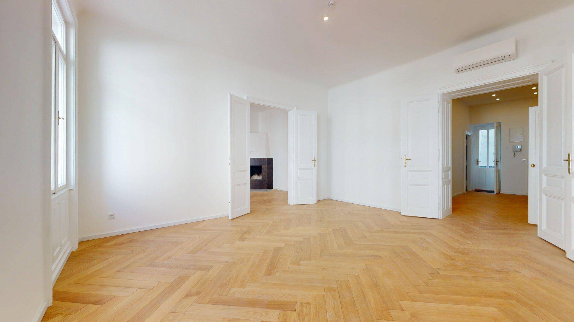 Großzügiges Wohnzimmer mit Fischgrätparkett, Klimaanlage und Blick auf den modernen Kamin.
