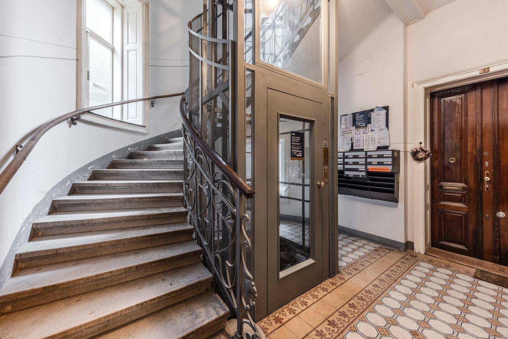Historisches Treppenhaus mit modernem Aufzug und dekorativen Fliesen, das den Charme des Altbaus bewahrt.