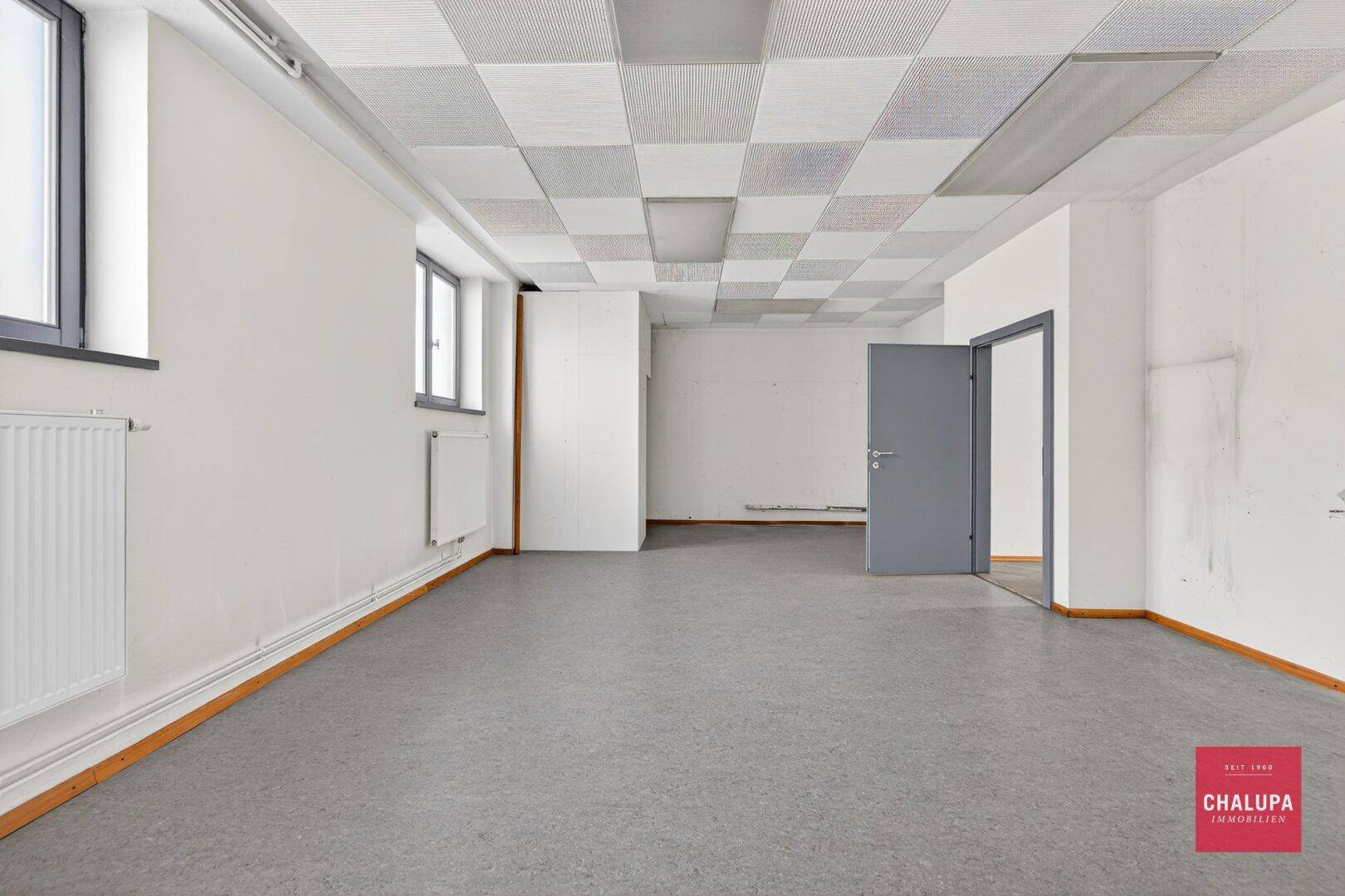 Großer, leerer Raum mit Rasterdeckenplatten und mehreren Fenstern.