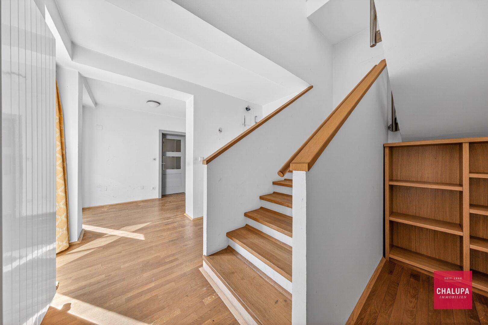 Heller Flur mit Holztreppe und Geländer, der zu den oberen Etagen führt.