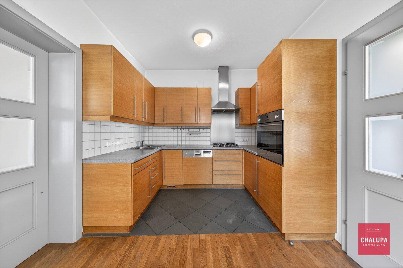 Funktionale Küche mit Holzschränken, Fliesenboden und integrierten Geräten.