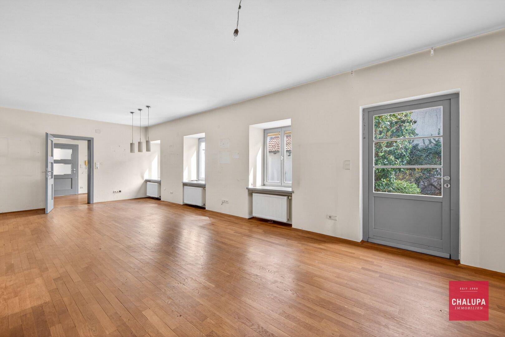 Helles Wohnzimmer mit Parkettboden und Zugang zu einem Außenbereich.