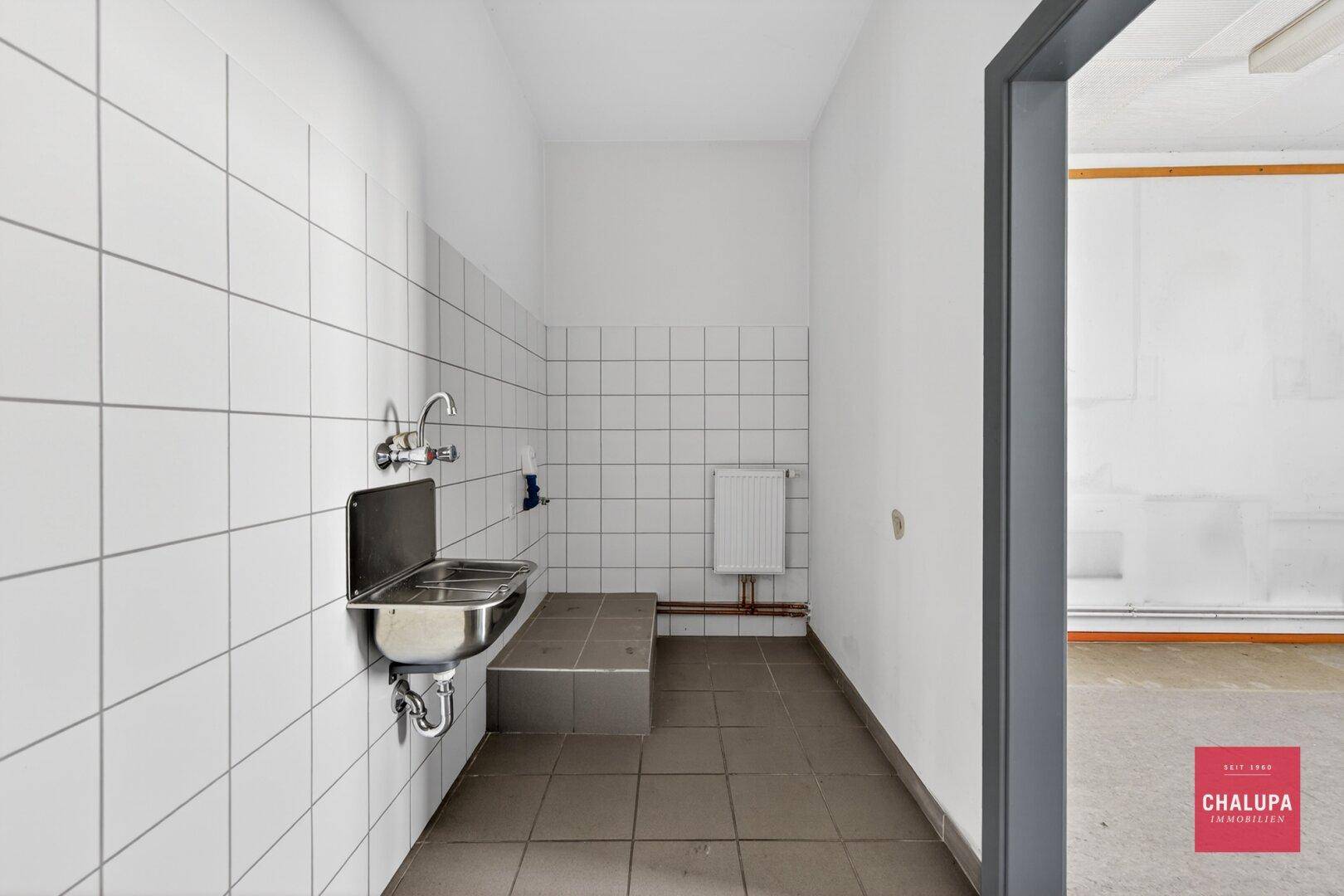 Einfacher Waschraum mit gefliesten Wänden, Edelstahlwaschbecken und Heizkörper.