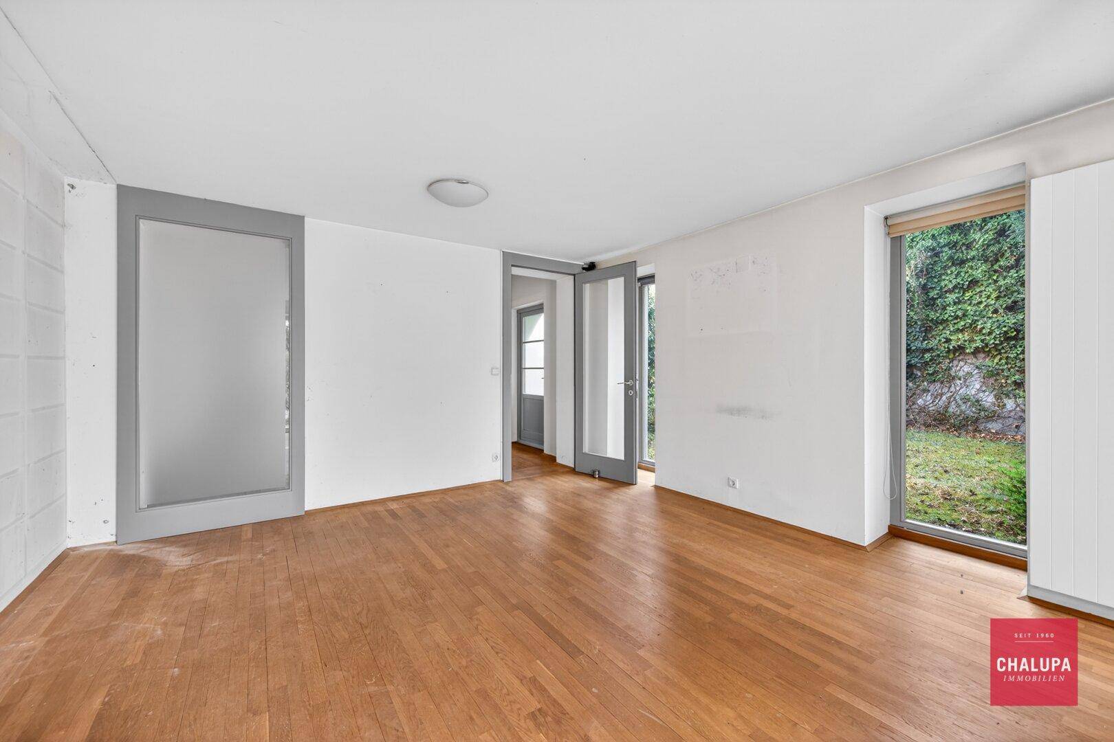 Heller Raum mit Parkettboden und Blick auf den Garten durch große Fenster.