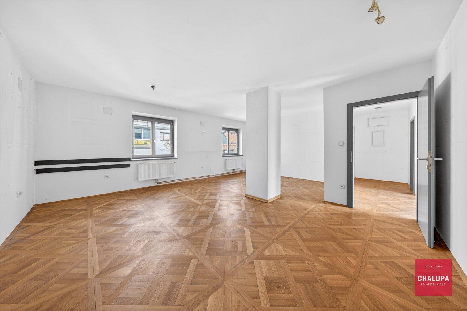 Großer, heller Raum mit kunstvollem Parkettboden und mehreren Fenstern.