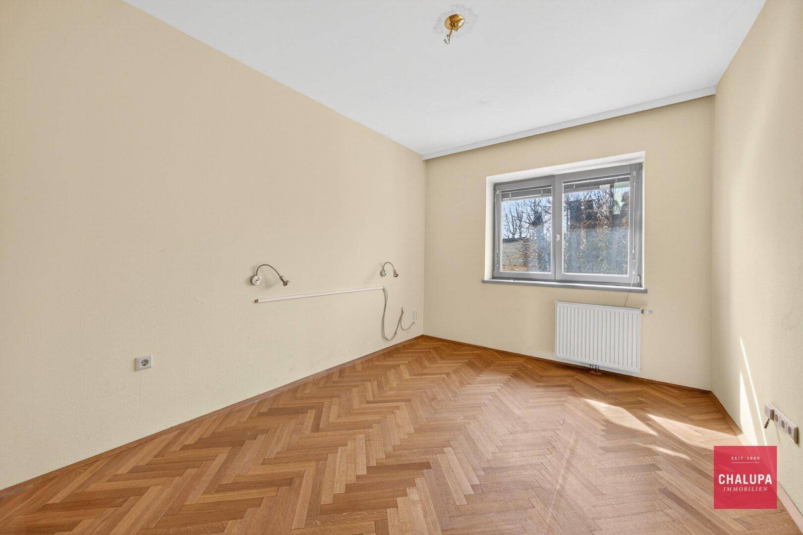 Helles Schlafzimmer mit gemustertem Parkettboden und einem Fenster.
