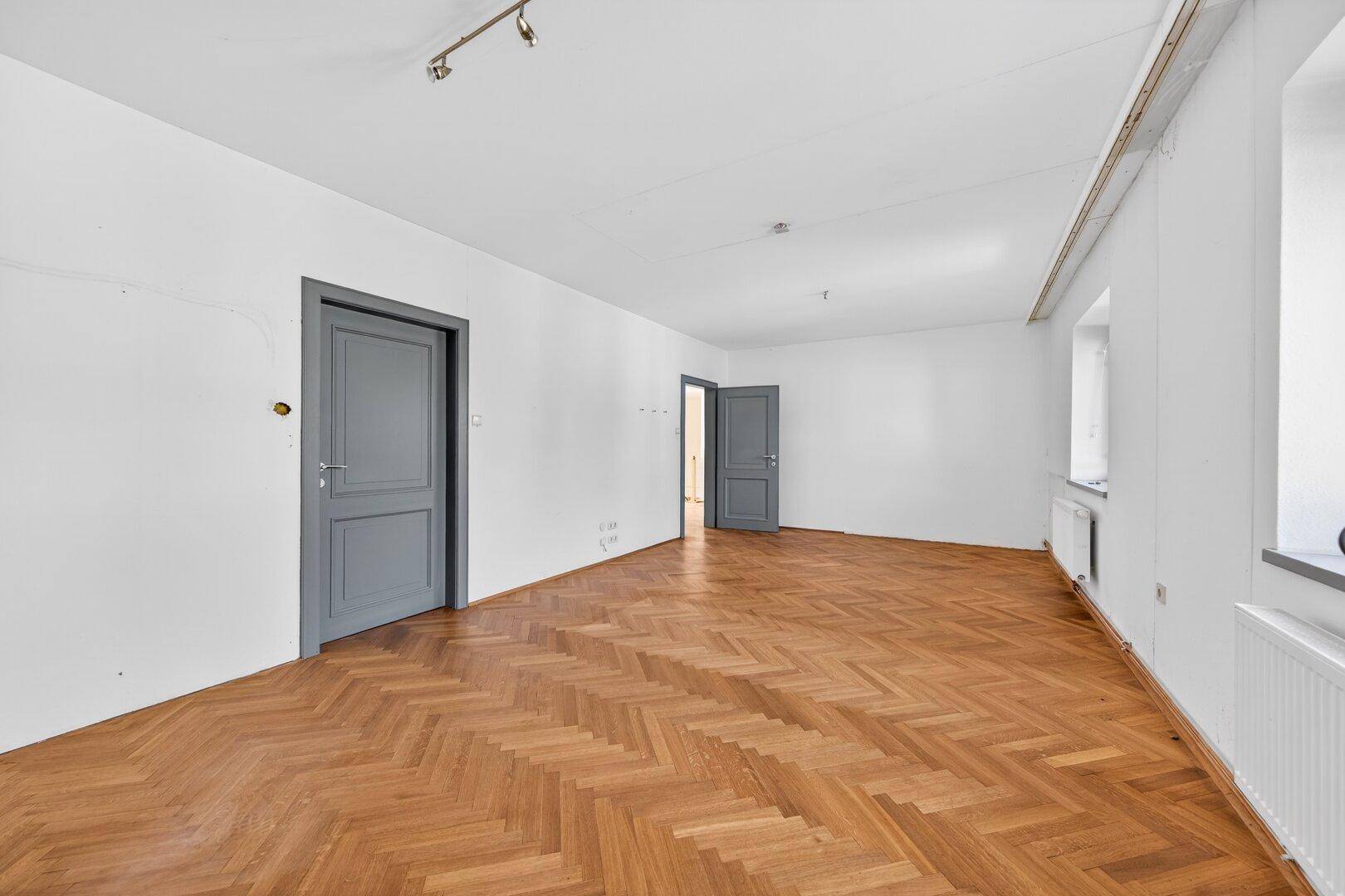 Geräumiger Raum mit gemustertem Parkettboden und mehreren Türen.