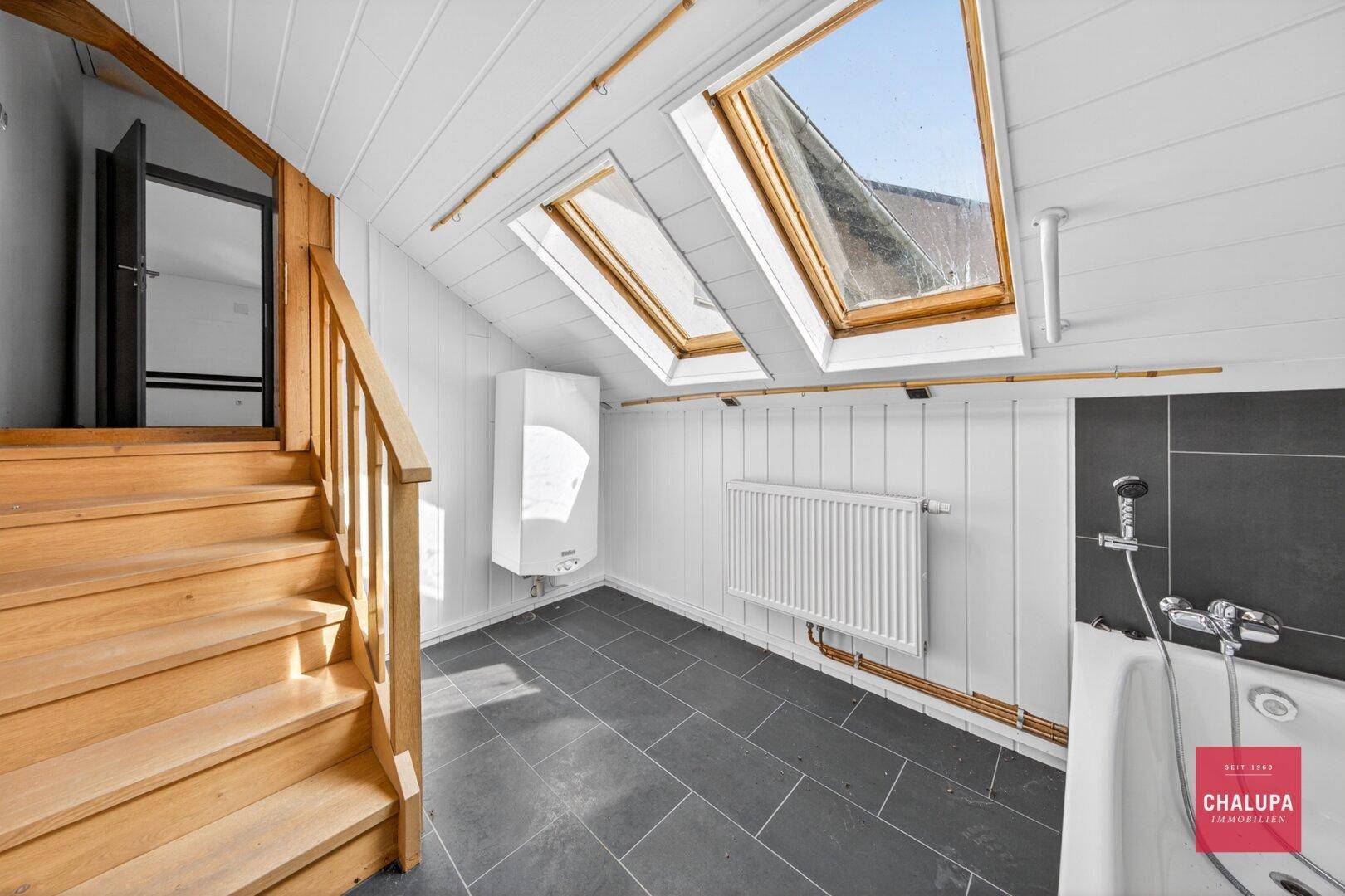 Ausgebauter Dachbodenbereich mit Holzverkleidung, Dachfenstern und Badewanne.