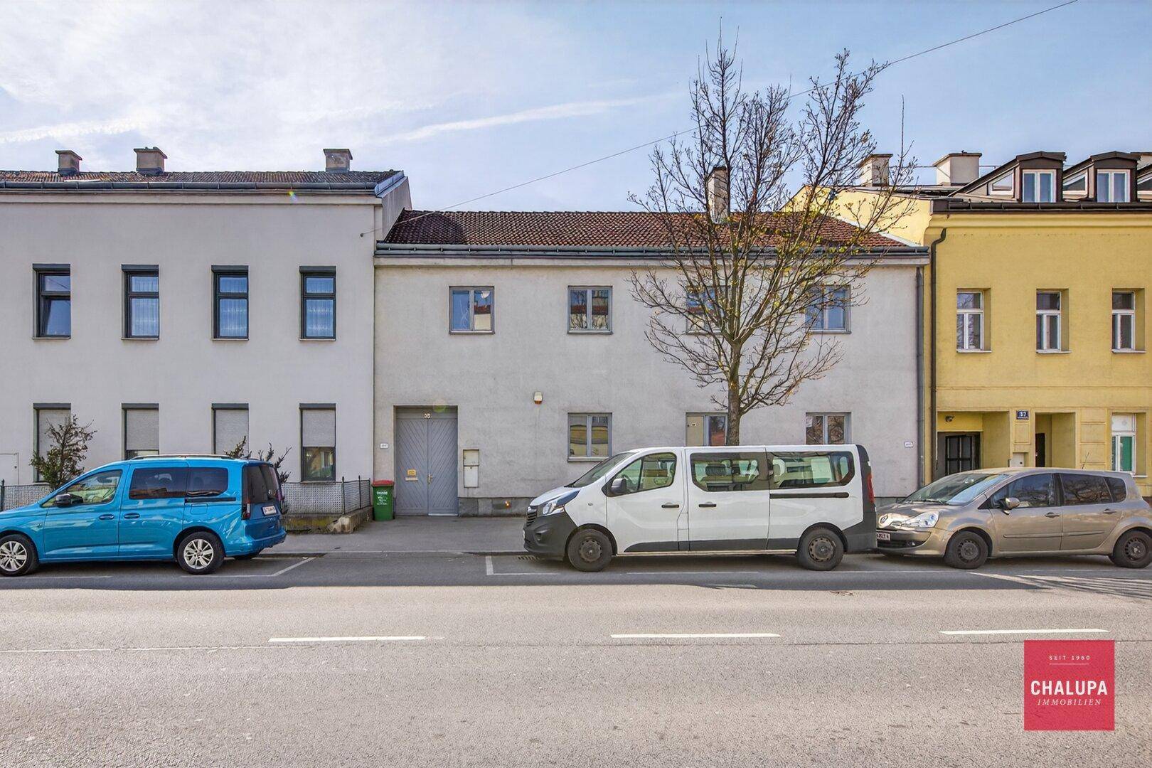 Ansicht der Gebäudefassade von der Straße mit parkenden Autos davor.