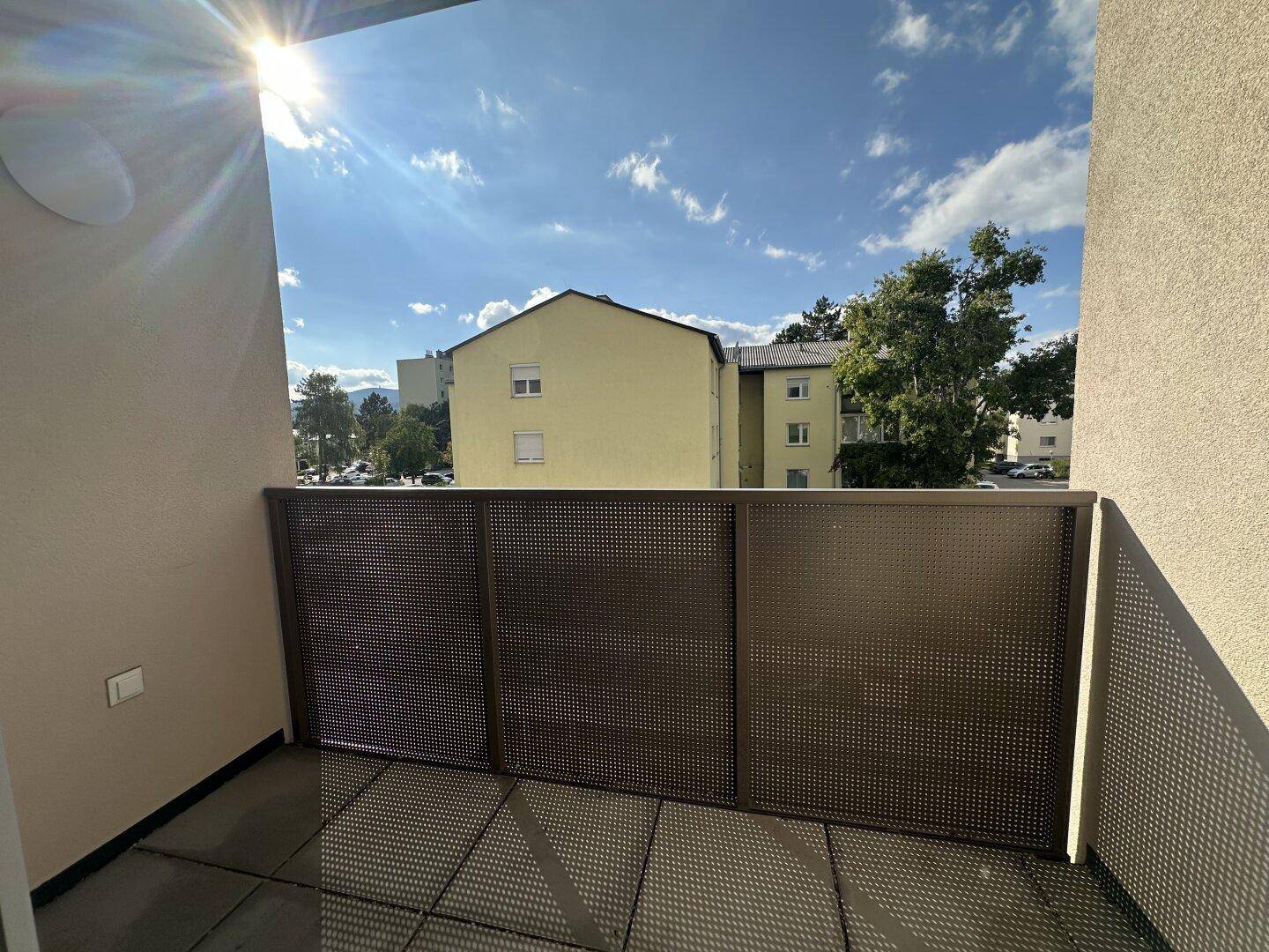 Sonniger Balkon mit Metallgeländer und Blick auf die umliegenden Gebäude und den blauen Himmel.