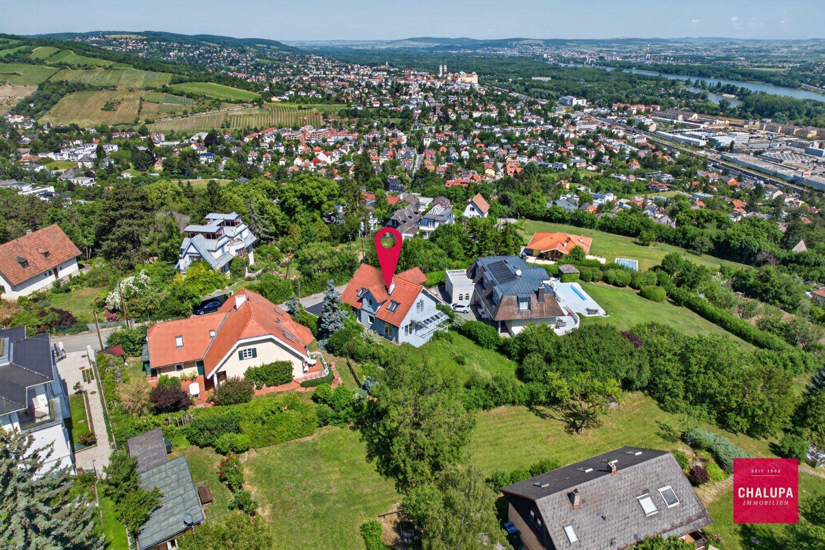 Weitläufige Luftaufnahme der Immobilie in einer grünen Wohngegend mit Flussblick.