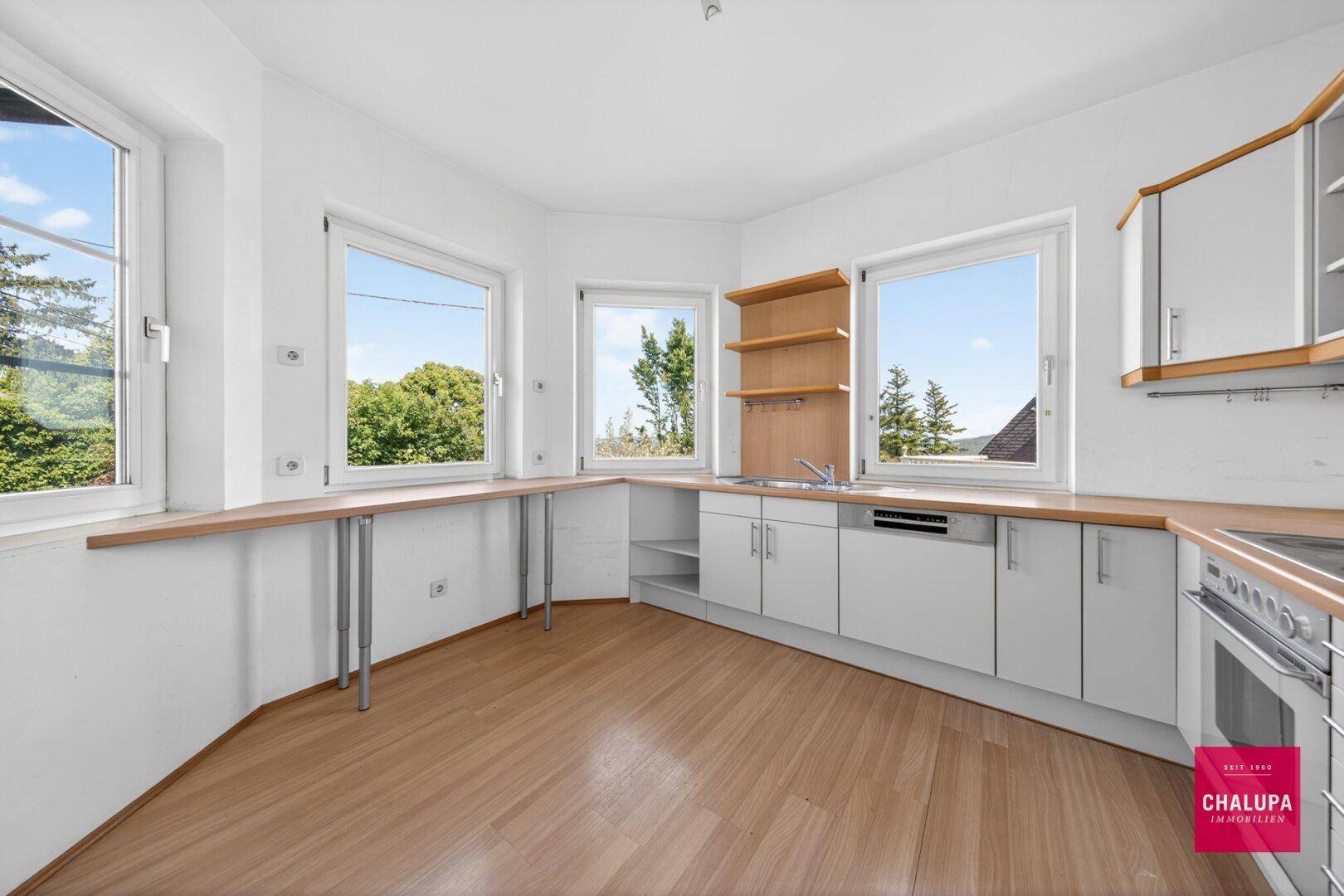 Helle Küche mit weißen Einbauschränken, Holztheke und weitem Ausblick ins Grüne.