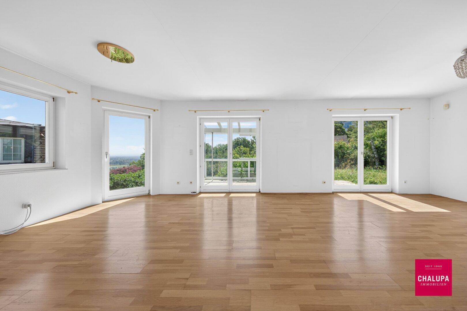 Lichtdurchfluteter Wohnbereich mit Holzboden und mehreren Fenstertüren zum Garten.