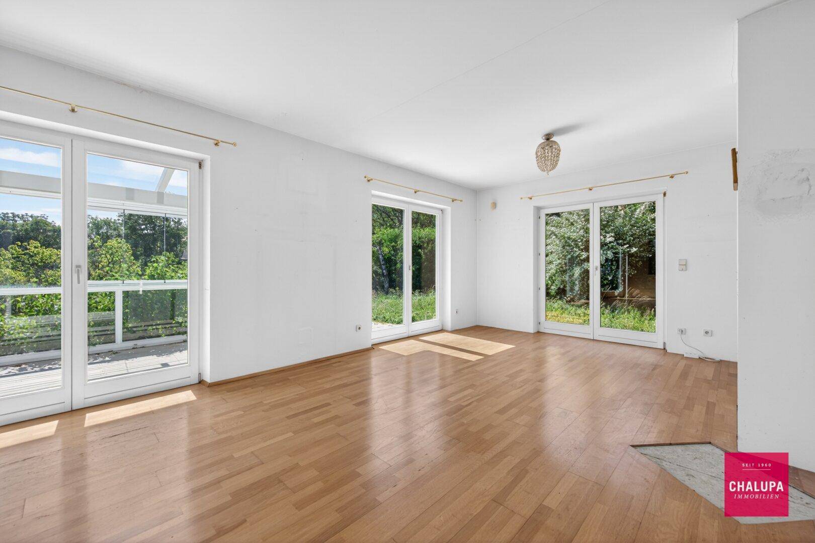 Heller Wohnraum mit Holzboden, großen Fenstern und Zugang zu einem Außenbereich.