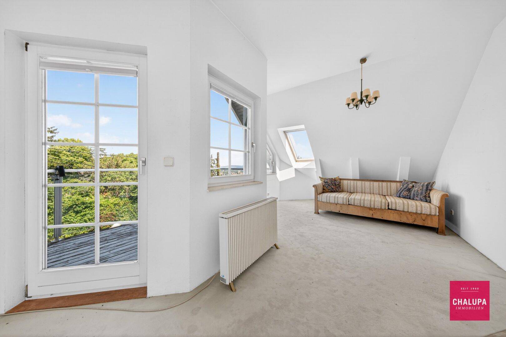 Gemütlicher Dachgeschossraum mit Teppichboden, Sofa und Zugang zu einem Balkon.