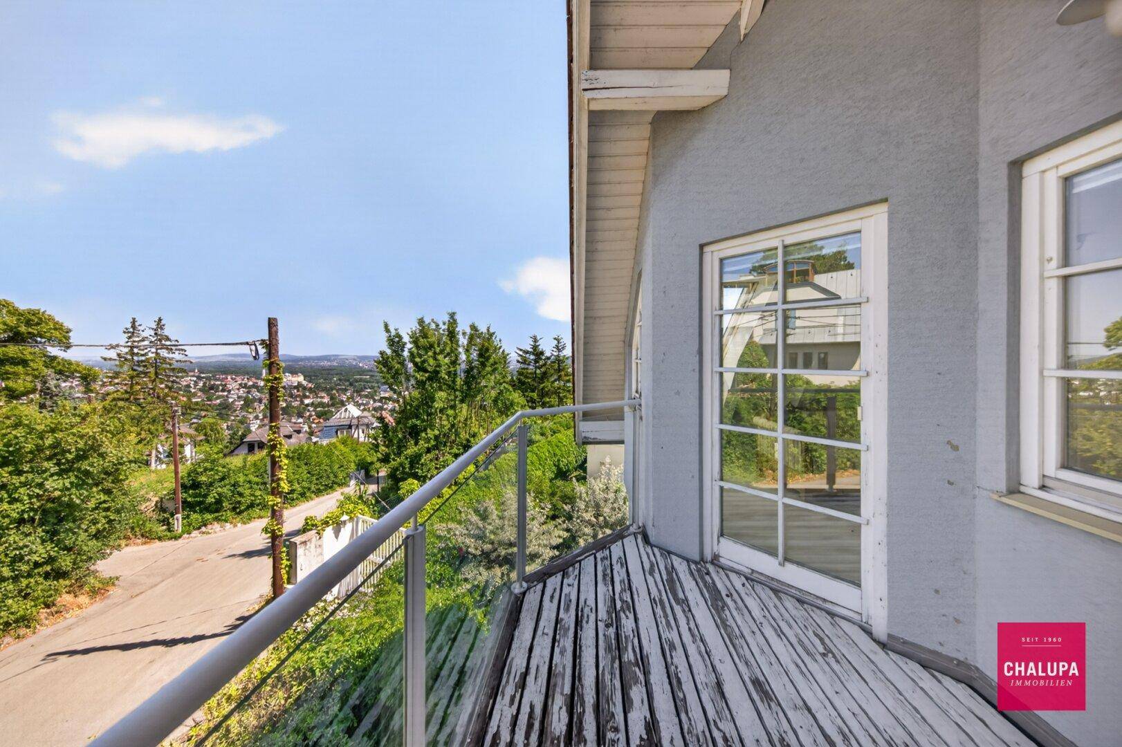 Kleiner Balkon mit Holzboden und Metallgeländer, bietet Blick auf die Straße und Bäume.