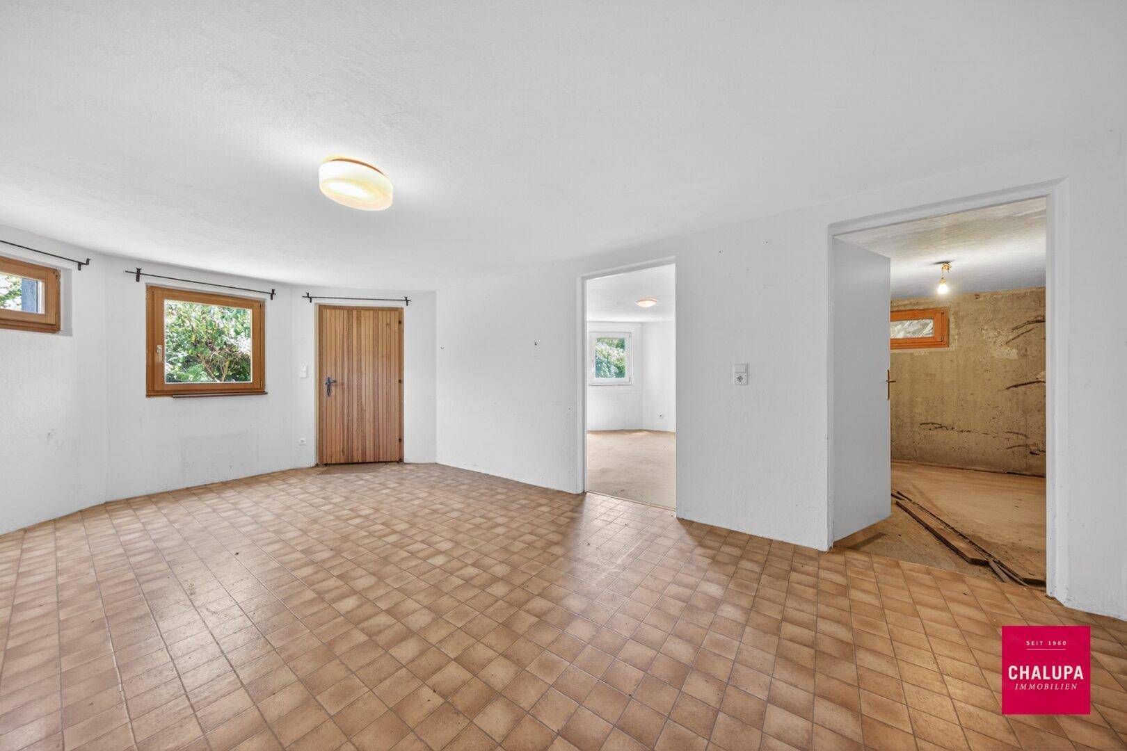 Helles Kellerzimmer mit Fliesenboden und Zugang zu weiteren Räumen.