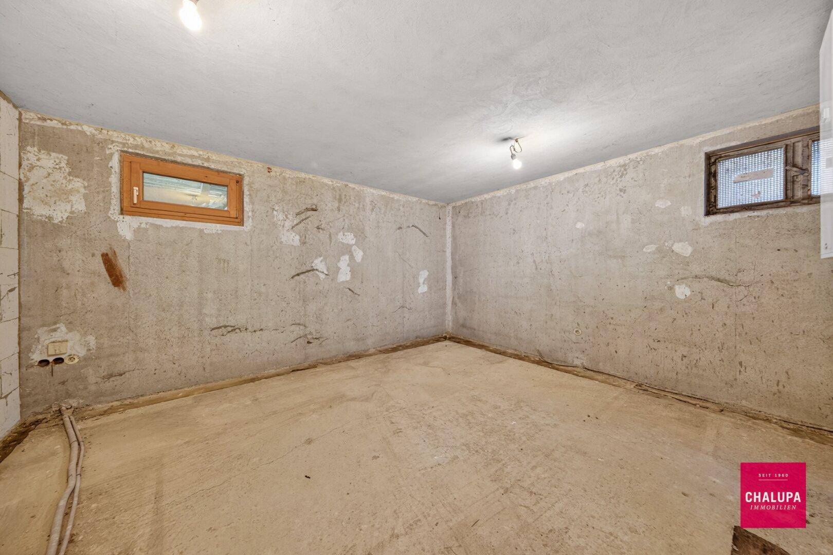 Unfertiger Kellerraum mit Betonwänden und kleinen Fenstern, ideal als Abstellraum.