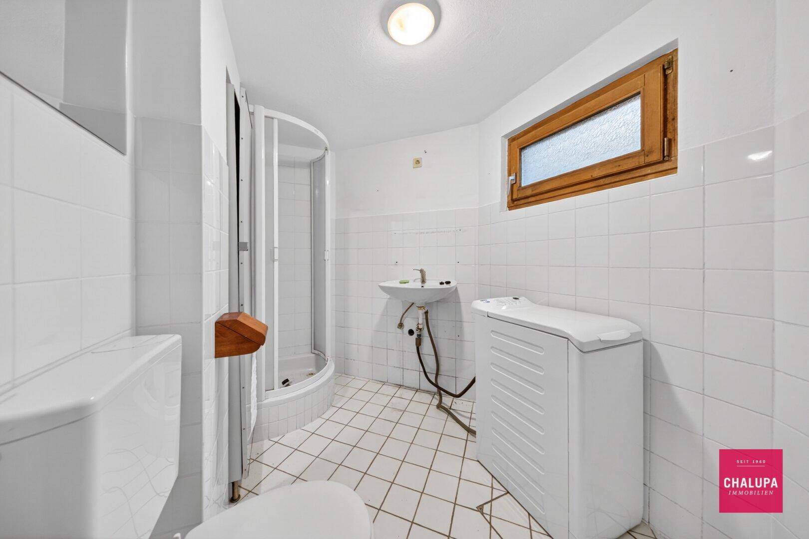 Einfaches Badezimmer im Keller mit Dusche, WC und Waschmaschine.