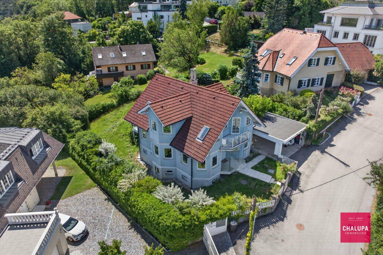 Luftaufnahme des Hauses mit rotem Ziegeldach und umliegenden Gärten in hügeliger Landschaft.