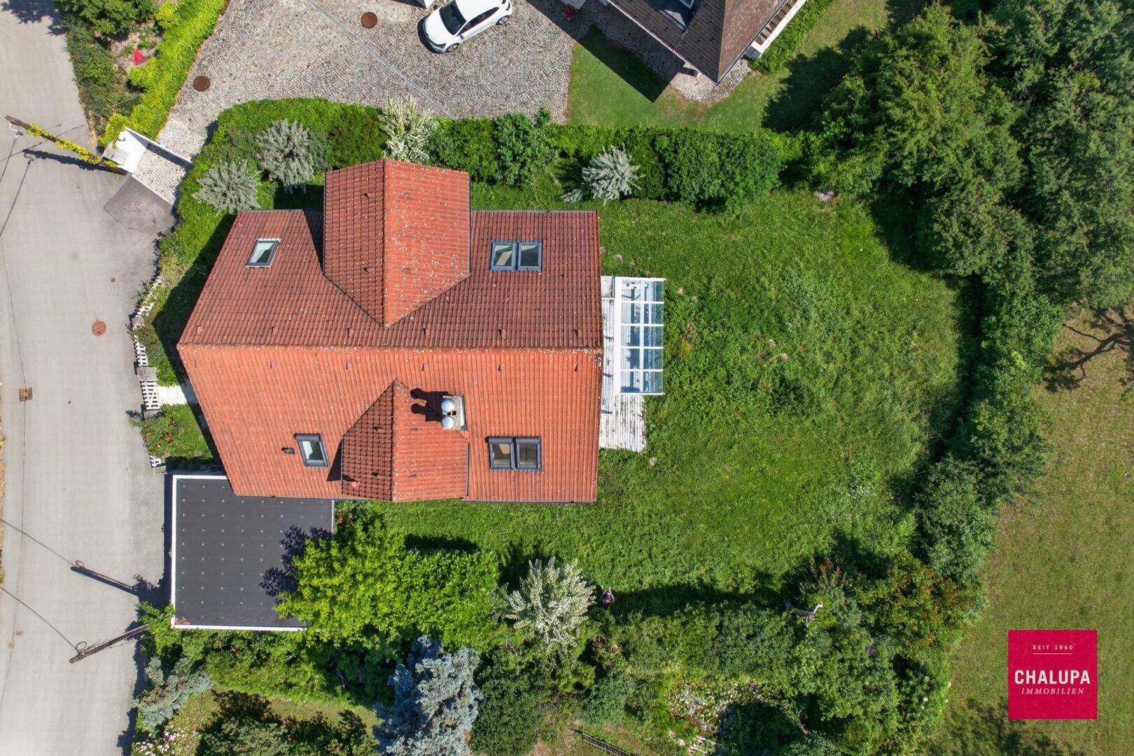 Draufsicht des Grundstücks mit Haus, Garten, Carport und angrenzender Straße.