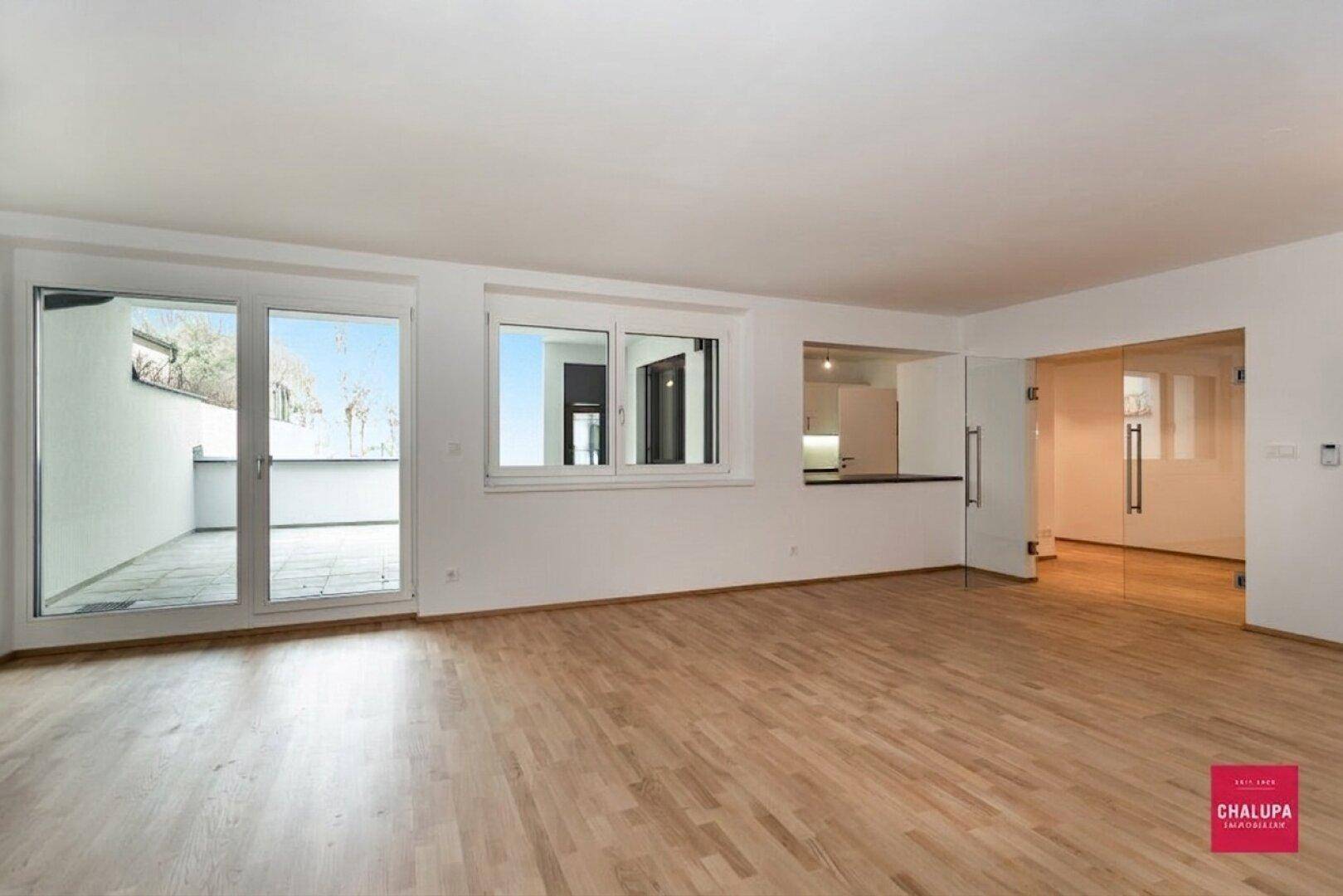 Helles Wohnzimmer mit Parkettboden, großen Glastüren zur Terrasse und Durchreiche zur Küche.