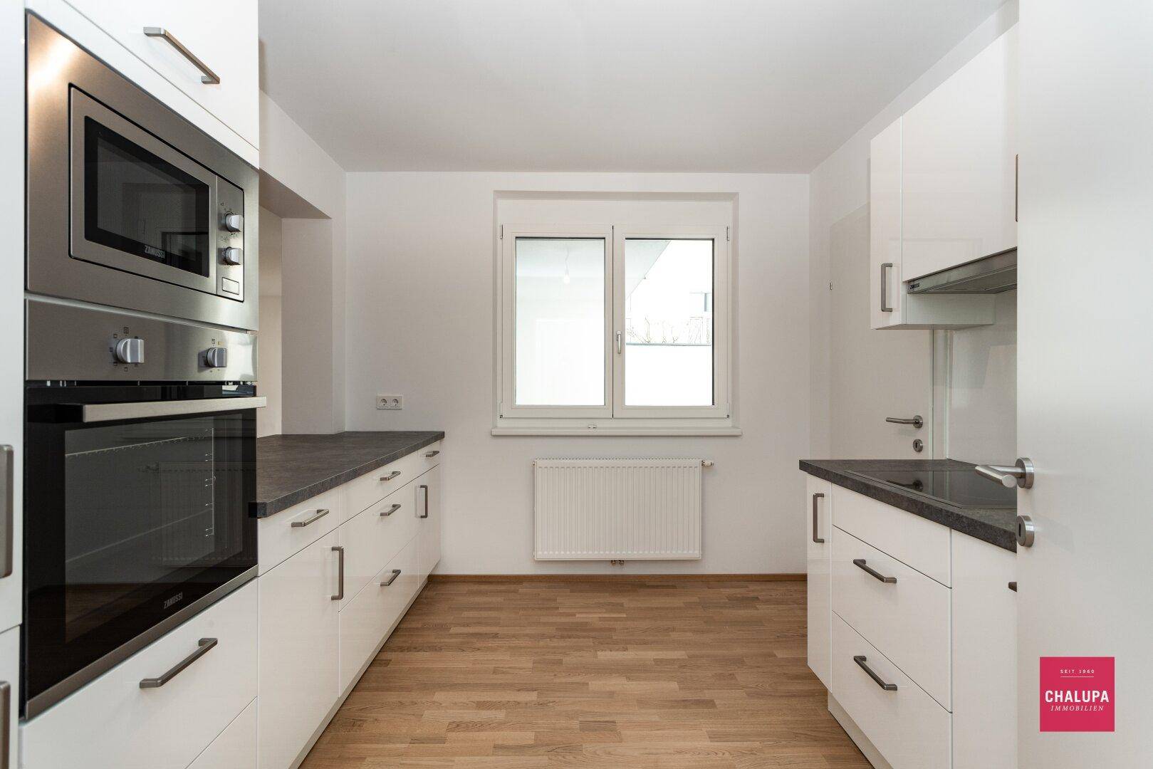 Moderne Küche mit weißen Schränken, dunklen Arbeitsplatten und integrierten Geräten.